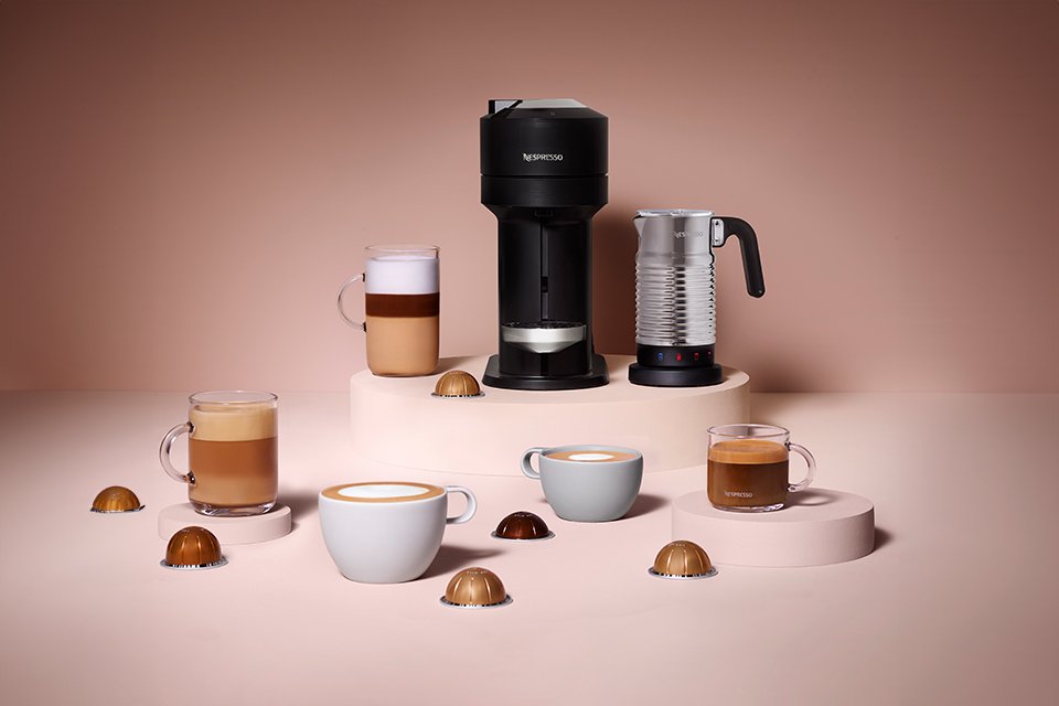 A Nespresso coffee machine with a set of coffee cups and capsules around it.